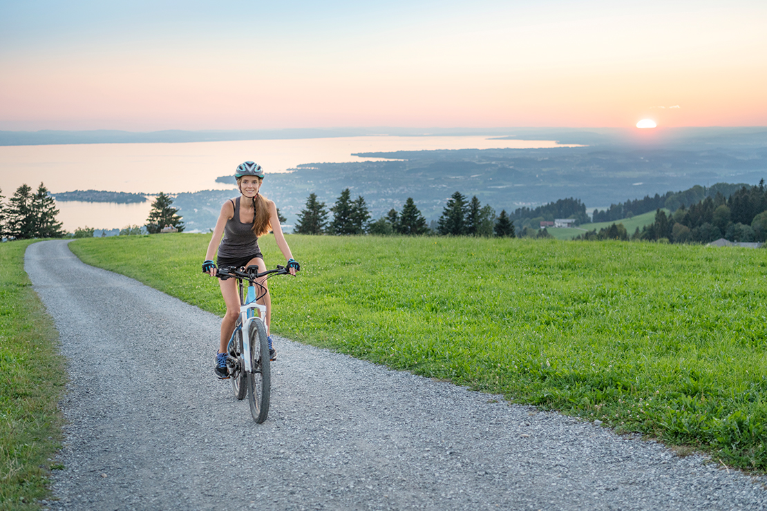 Mountainbiken, auch im Kurzurlaub: Frau fährt mit Fahrrad oberhalb des Bodensees entlang
