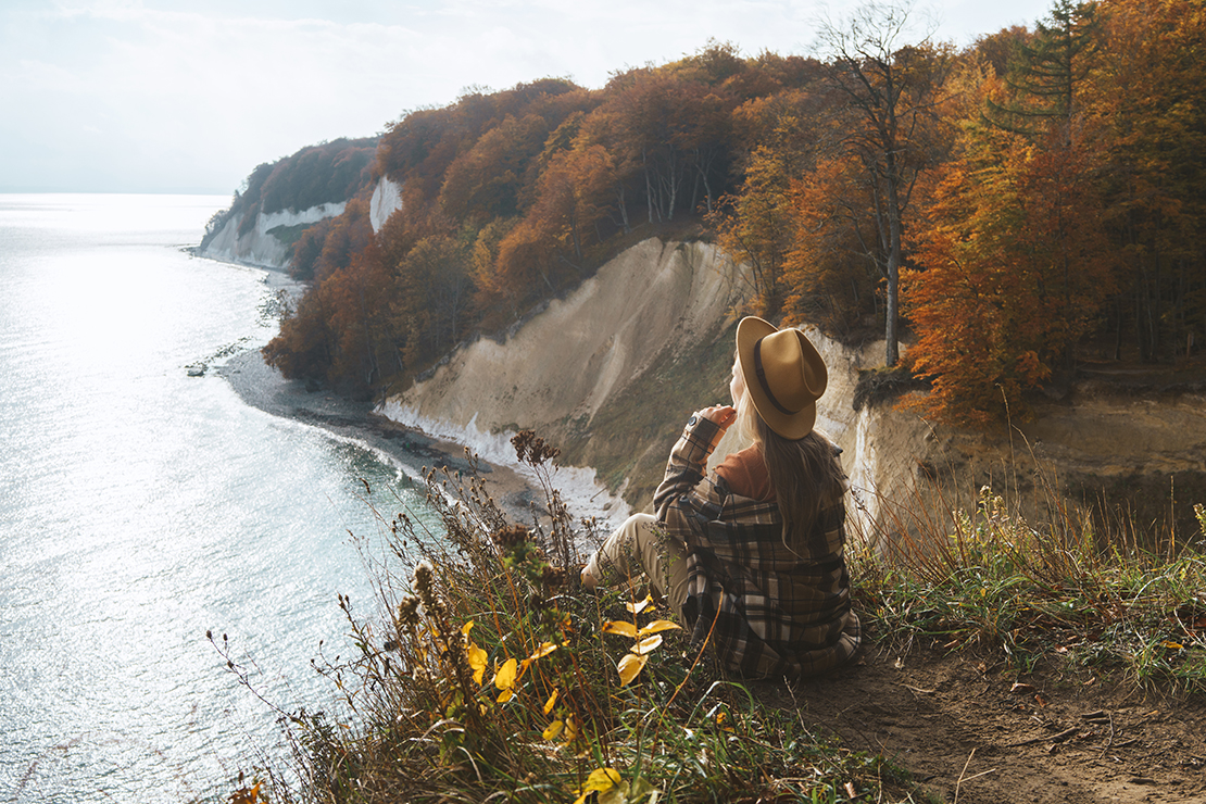 Frau sitzt auf Steilküste am Strand bei Besuch auf Rügen